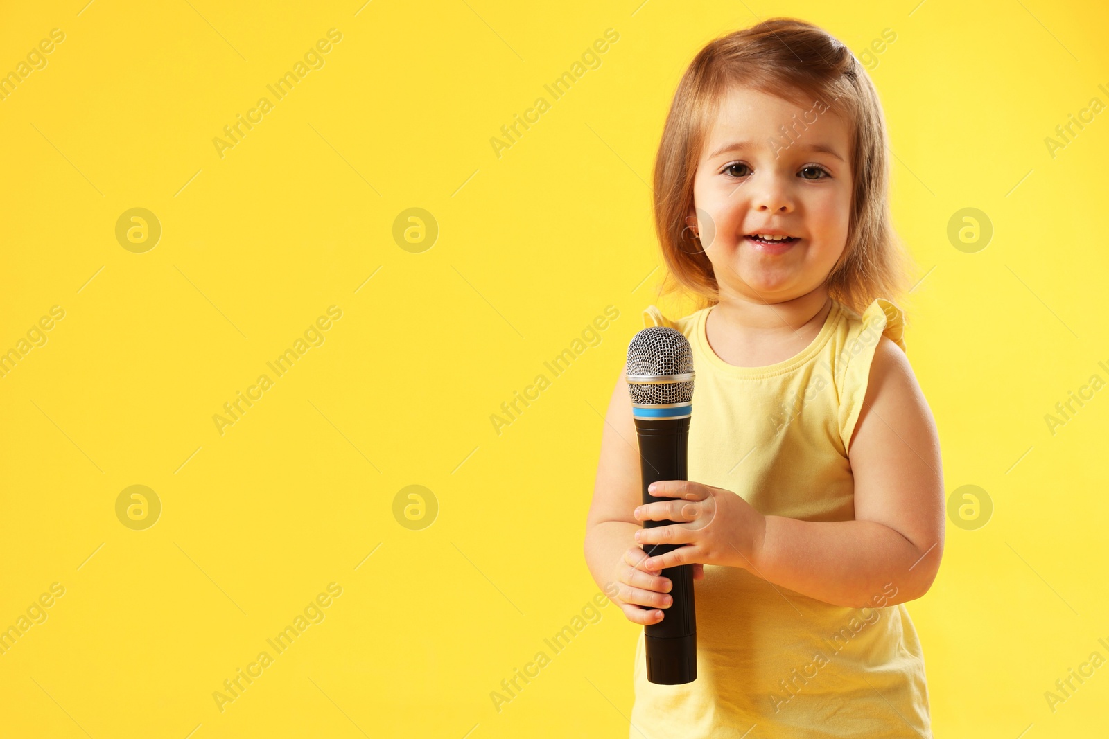 Cute little girl with microphone on yellow background, space for text Photo of Cute little girl with microphone on yellow background, space for text