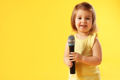 Photo of Cute little girl with microphone on yellow background, space for text