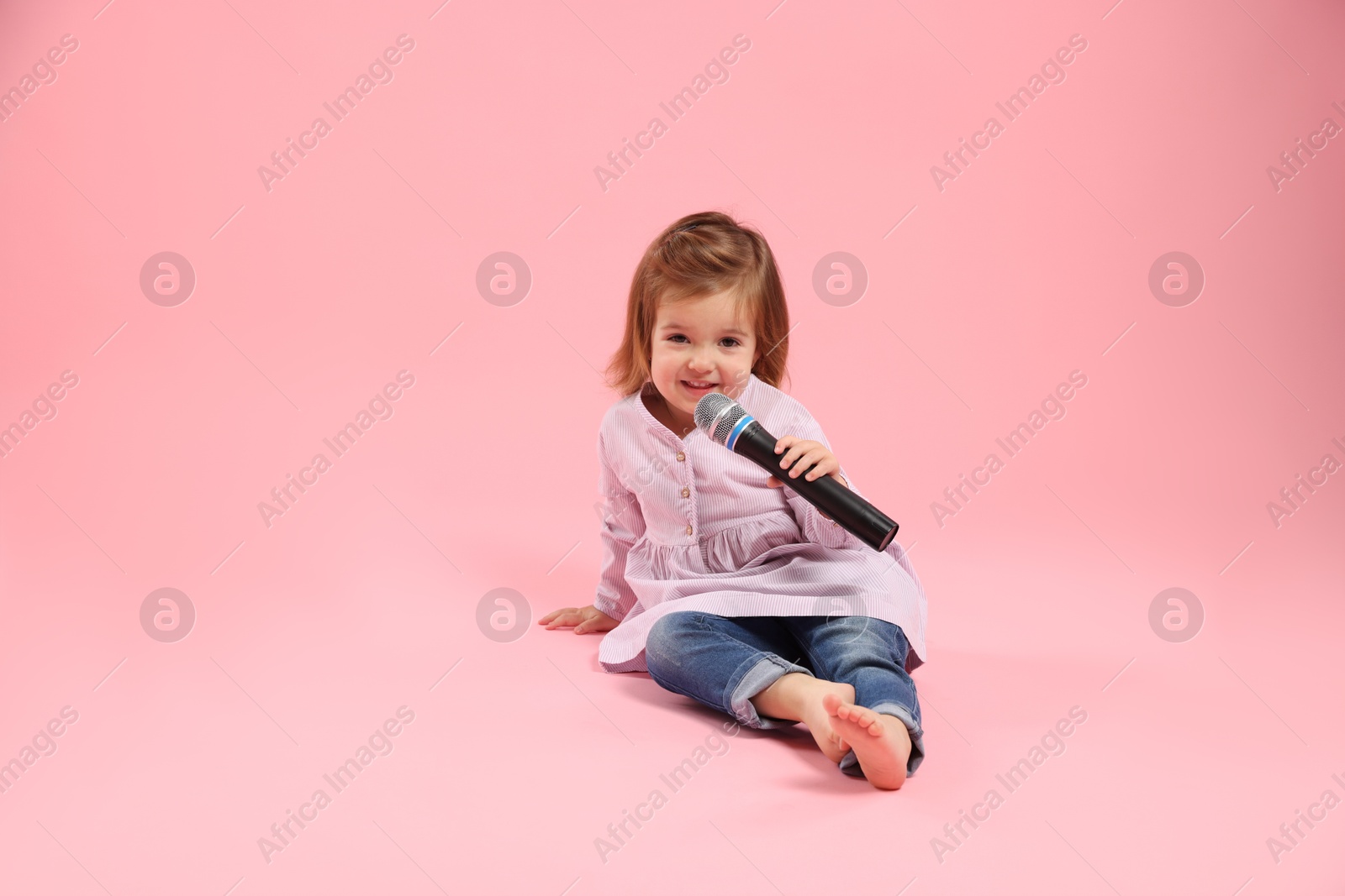 Cute little girl with microphone on pink background Photo of Cute little girl with microphone on pink background