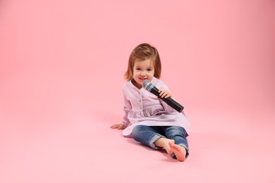 Photo of Cute little girl with microphone on pink background