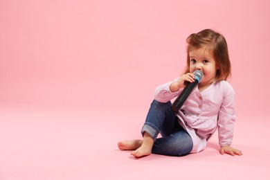 Photo of Cute little girl with microphone on pink background, space for text