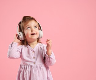 Photo of Cute little girl in headphones on pink background, space for text