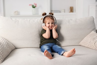 Photo of Cute little girl in headphones on sofa at home