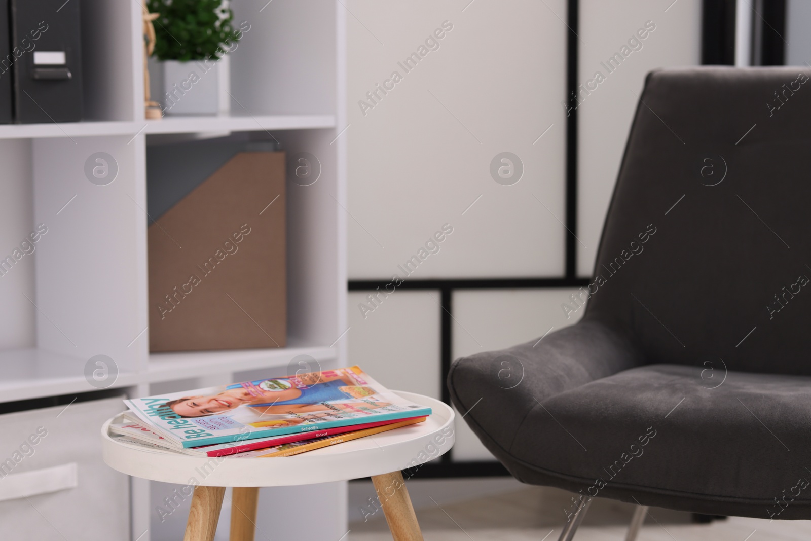 Different trendy magazines on white table and armchair indoors Photo of Different trendy magazines on white table and armchair indoors