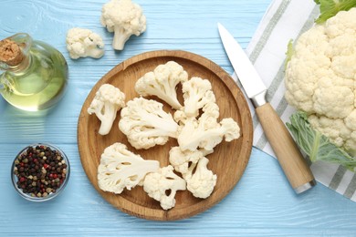 Photo of Pieces of cauliflower, peppercorns, oil and knife on light blue wooden table, flat lay