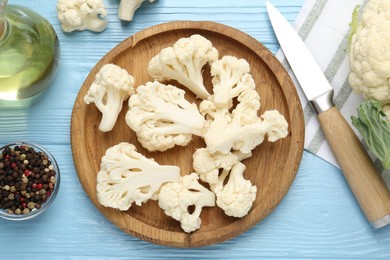 Photo of Pieces of cauliflower, peppercorns, oil and knife on light blue wooden table, flat lay
