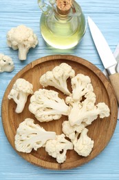 Photo of Pieces of cauliflower, oil and knife on light blue wooden table, flat lay