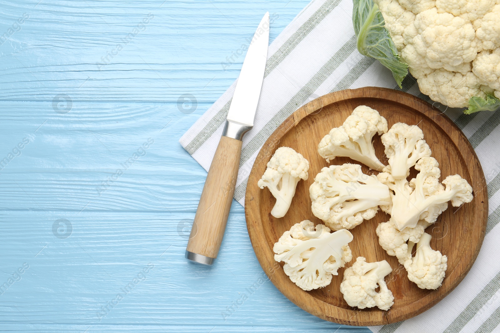 Pieces of cauliflower and knife on light blue wooden table, flat lay. Space for text Photo of Pieces of cauliflower and knife on light blue wooden table, flat lay. Space for text