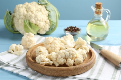 Photo of Pieces of cauliflower, peppercorns, oil and knife on light blue wooden table