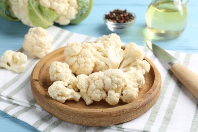 Photo of Pieces of cauliflower, peppercorns, oil and knife on light blue wooden table, closeup