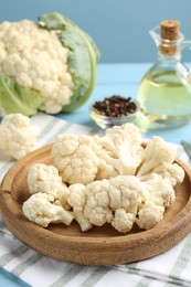 Photo of Pieces of cauliflower, peppercorns and oil on light blue wooden table, closeup