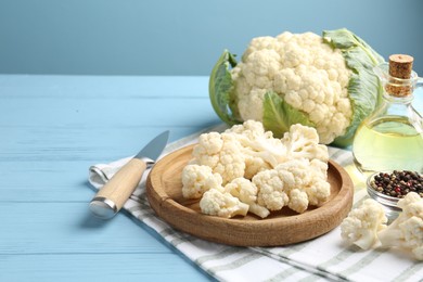 Photo of Pieces of cauliflower, peppercorns, oil and knife on light blue wooden table. Space for text