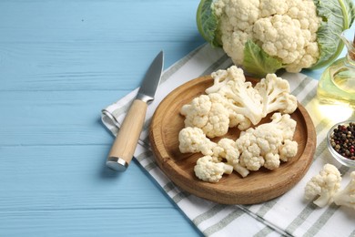 Photo of Pieces of cauliflower, peppercorns, oil and knife on light blue wooden table. Space for text