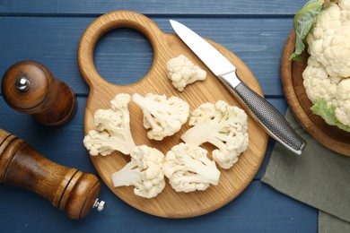 Photo of Pieces of cauliflower, knife and spices on blue wooden table, flat lay