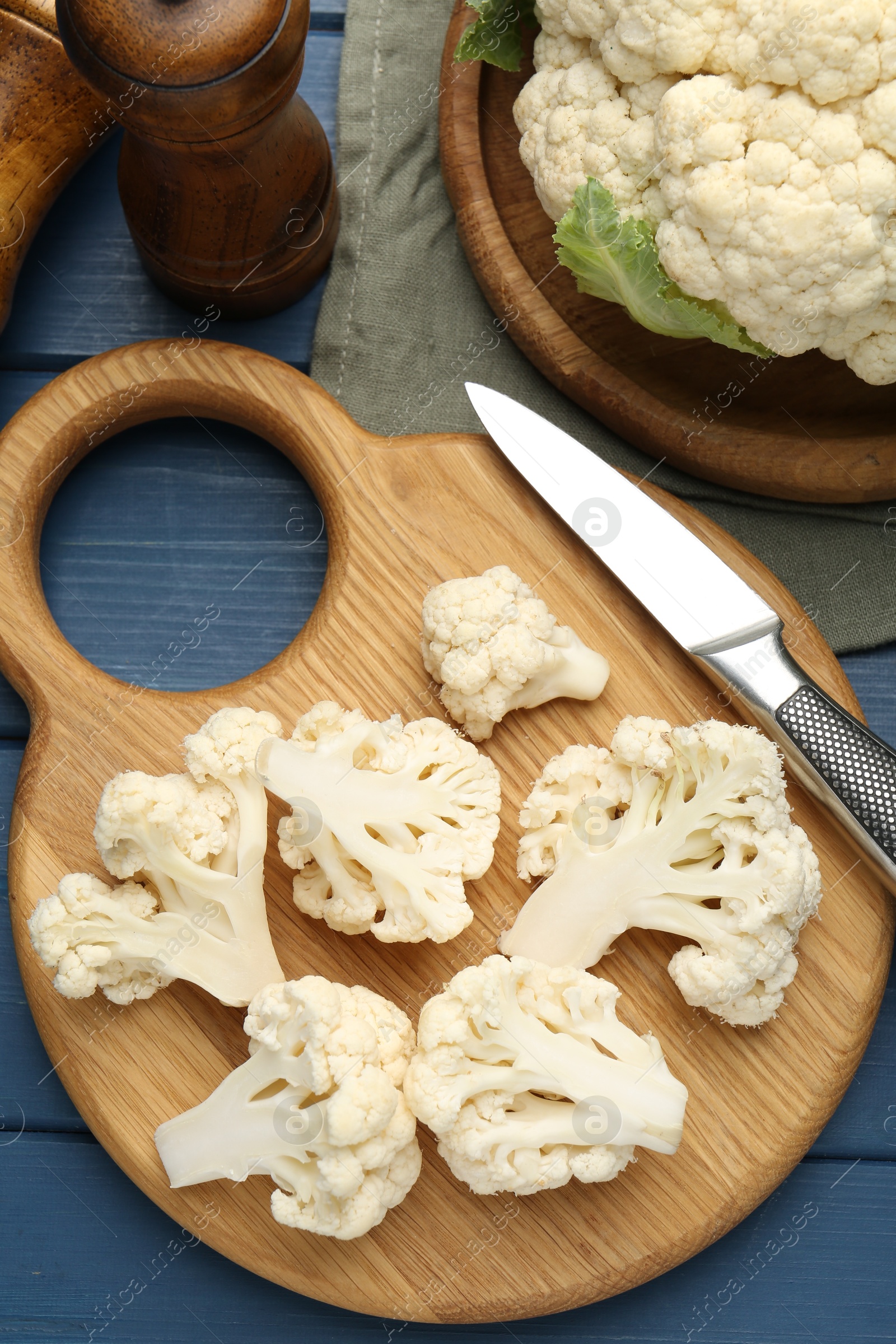 Pieces of cauliflower, knife and spices on blue wooden table, flat lay Photo of Pieces of cauliflower, knife and spices on blue wooden table, flat lay