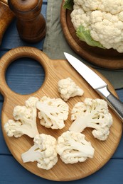 Photo of Pieces of cauliflower, knife and spices on blue wooden table, flat lay