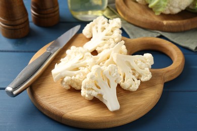 Photo of Pieces of cauliflower, knife and spices on blue wooden table, closeup