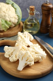 Photo of Pieces of cauliflower, knife and spices on blue wooden table, closeup