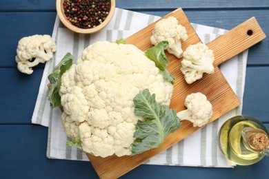 Photo of Raw cauliflower, peppercorns and oil on blue wooden table, flat lay