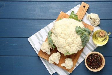 Photo of Raw cauliflower, peppercorns and oil on blue wooden table, flat lay. Space for text
