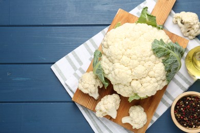 Photo of Raw cauliflower, peppercorns and oil on blue wooden table, flat lay. Space for text