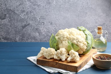 Photo of Raw cauliflower, peppercorns and oil on blue wooden table. Space for text