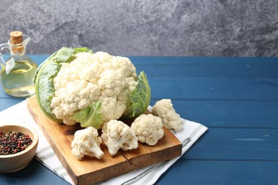 Photo of Raw cauliflower, peppercorns and oil on blue wooden table. Space for text