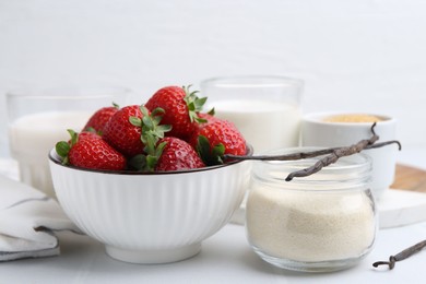 Photo of Different ingredients for panna cotta. Milk, sugar, vanilla and strawberries on white tiled table, closeup