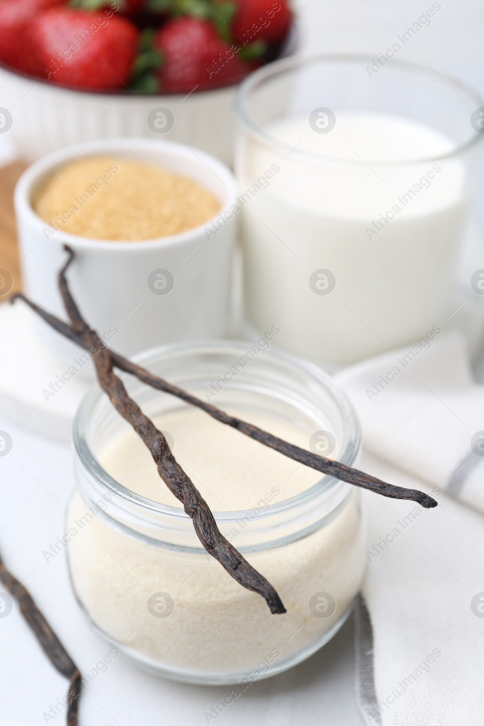 Photo of Different ingredients for panna cotta. Milk, sugar, vanilla and strawberries on white tiled table, closeup