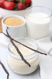 Photo of Different ingredients for panna cotta. Milk, sugar, vanilla and strawberries on white tiled table, closeup