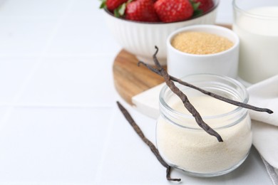 Photo of Different ingredients for panna cotta. Milk, sugar, vanilla and strawberries on white tiled table, closeup. Space for text