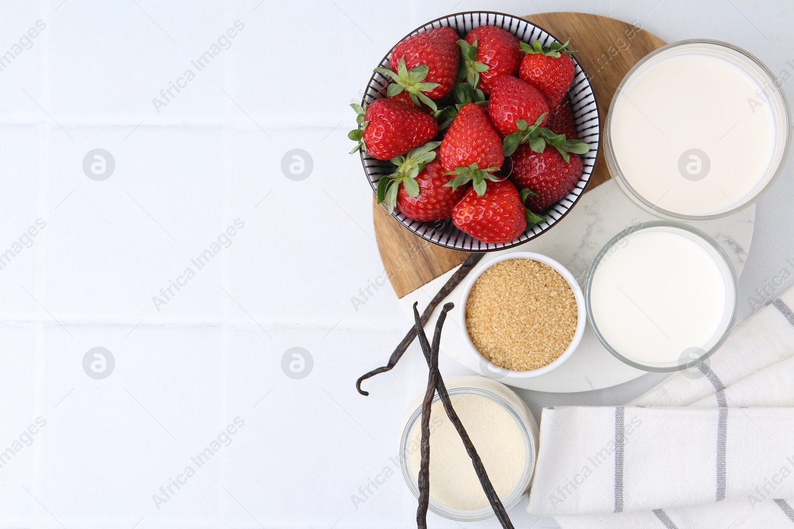 Different ingredients for panna cotta. Milk, sugar, vanilla and strawberries on white tiled table, flat lay. Space for text Photo of Different ingredients for panna cotta. Milk, sugar, vanilla and strawberries on white tiled table, flat lay. Space for text