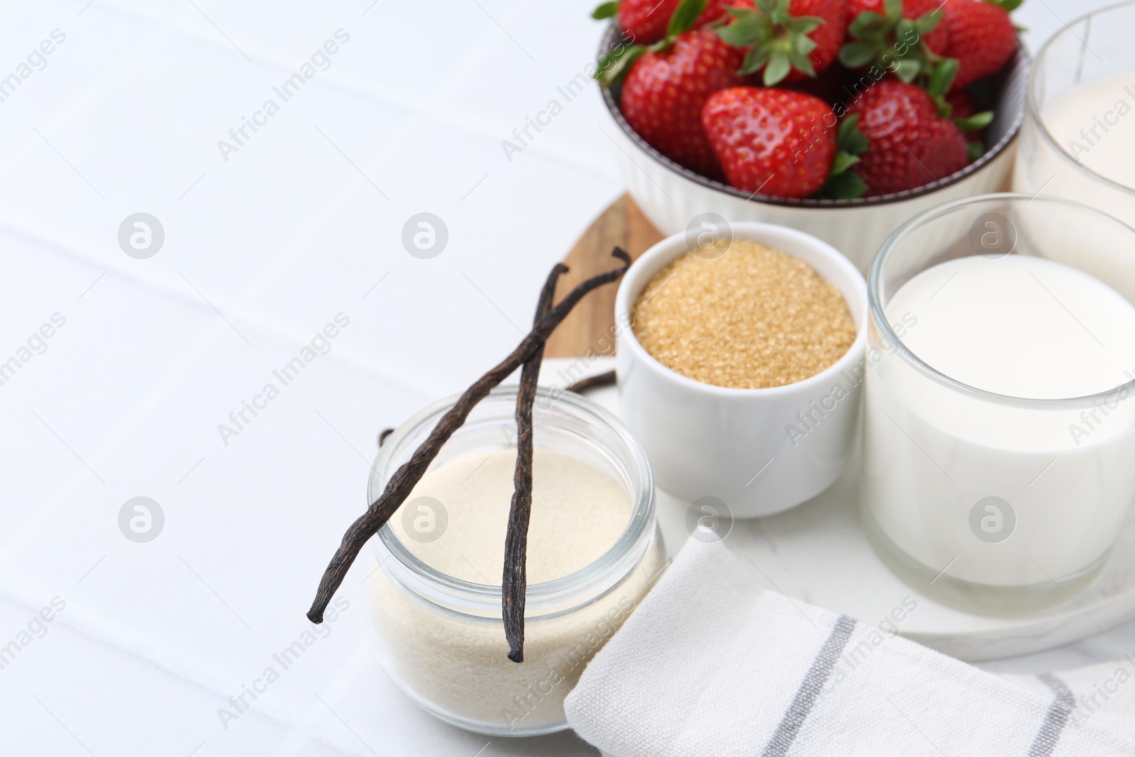 Photo of Different ingredients for panna cotta. Milk, sugar, vanilla and strawberries on white tiled table, closeup