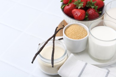 Photo of Different ingredients for panna cotta. Milk, sugar, vanilla and strawberries on white tiled table, closeup