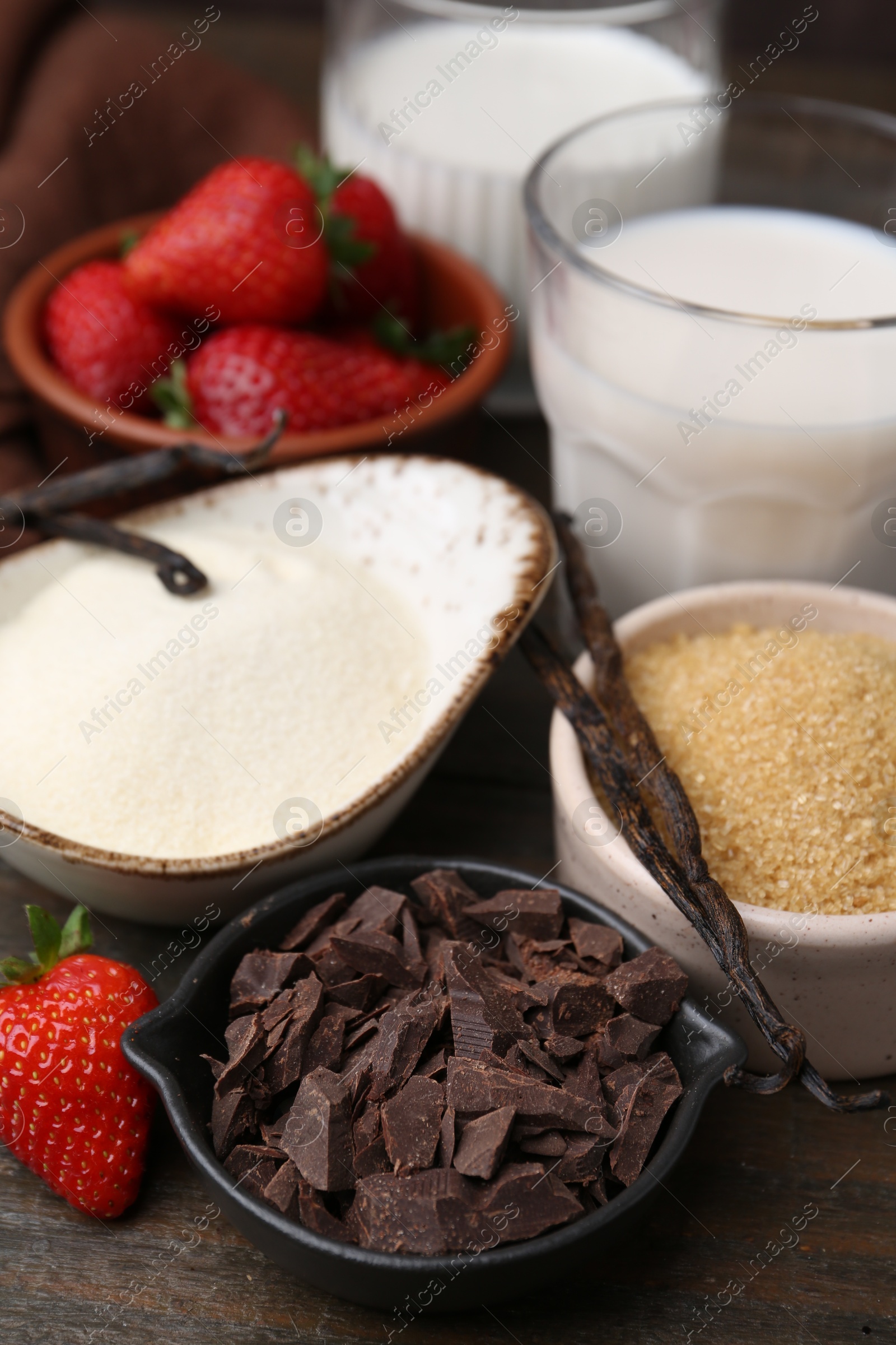Photo of Different ingredients for panna cotta. Milk, sugar, vanilla, chocolate and strawberries on wooden table, closeup