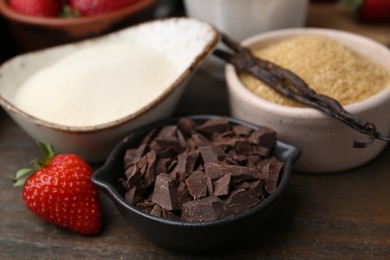 Photo of Different ingredients for panna cotta. Milk, sugar, vanilla, chocolate and strawberries on wooden table, closeup