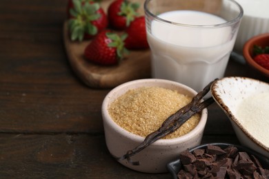 Photo of Different ingredients for panna cotta. Milk, sugar, vanilla, chocolate and strawberries on wooden table, closeup. Space for text