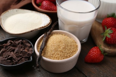 Photo of Different ingredients for panna cotta. Milk, sugar, vanilla, chocolate and strawberries on wooden table, closeup
