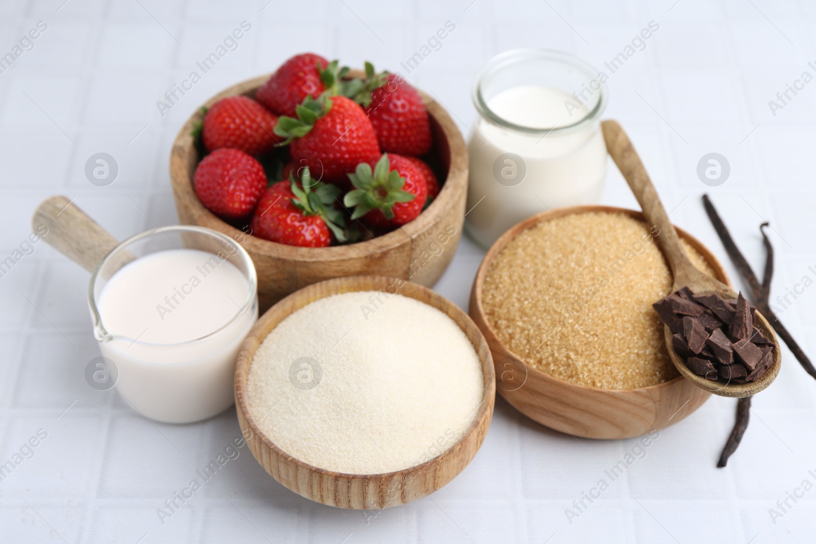 Different ingredients for panna cotta. Milk, sugar, vanilla, chocolate and strawberries on white tiled table, closeup Photo of Different ingredients for panna cotta. Milk, sugar, vanilla, chocolate and strawberries on white tiled table, closeup