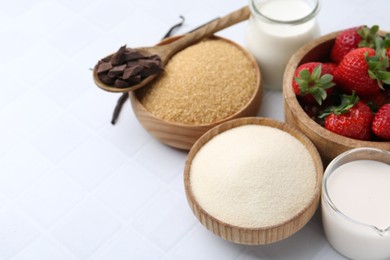Photo of Different ingredients for panna cotta. Milk, sugar, vanilla, chocolate and strawberries on white tiled table, closeup. Space for text