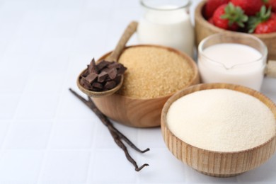 Photo of Different ingredients for panna cotta. Milk, sugar, vanilla, chocolate and strawberries on white tiled table, closeup. Space for text