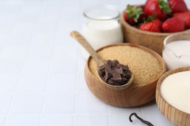 Photo of Different ingredients for panna cotta. Milk, sugar, vanilla, chocolate and strawberries on white tiled table, closeup. Space for text