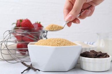 Photo of Making tasty panna cotta. Woman taking sugar with spoon at white table, closeup