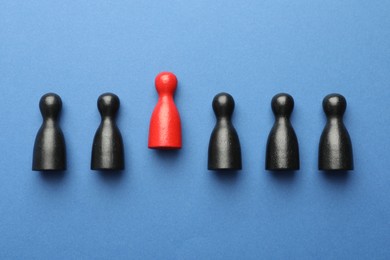 Photo of Unemployment. One red figure among black on blue background, flat lay