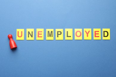 Photo of Word Unemployed and human figure on blue background, flat lay