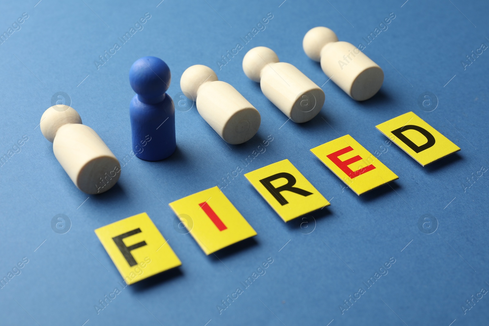 Dismissal. Word Fired and human figures on blue background, closeup Photo of Dismissal. Word Fired and human figures on blue background, closeup