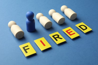 Photo of Dismissal. Word Fired and human figures on blue background, closeup