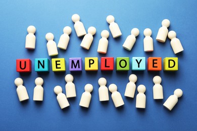 Photo of Word Unemployed and human figures on blue background, flat lay