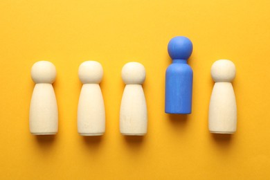 Photo of Unemployment. One blue figure among wooden on yellow background, flat lay
