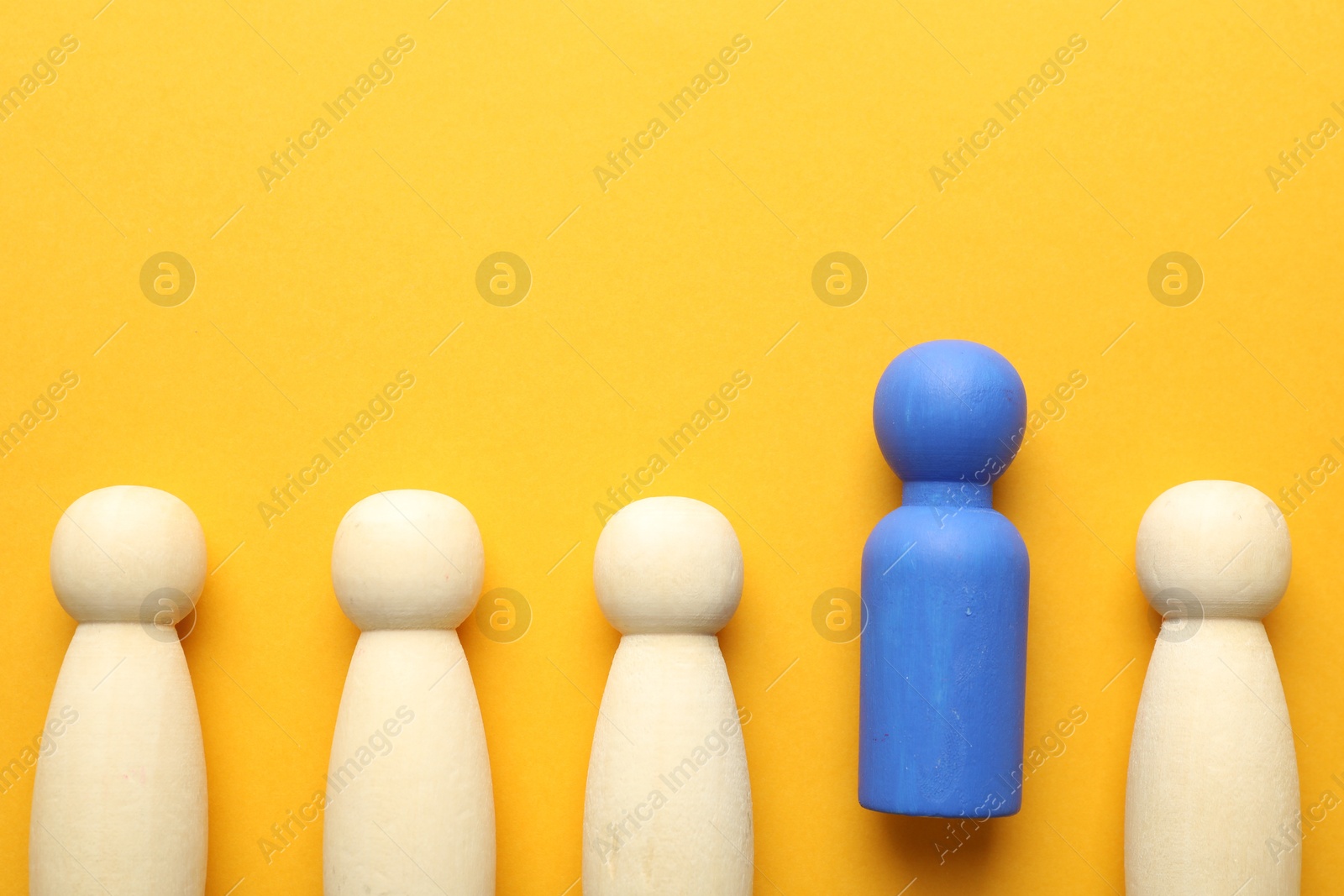 Unemployment. One blue figure among wooden on yellow background, flat lay. Space for text Photo of Unemployment. One blue figure among wooden on yellow background, flat lay. Space for text